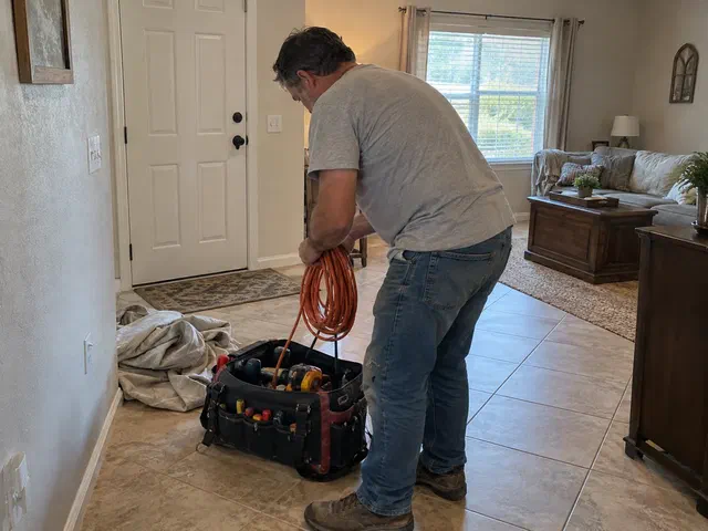 Handyman adjusting an interior door hinge in an ordinary stucco home with a drop cloth on the tile floor