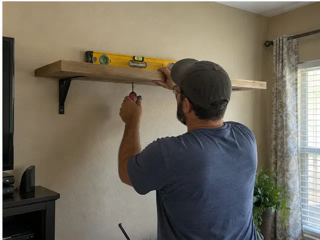 Handyman leveling and fastening a wood wall shelf in a family room