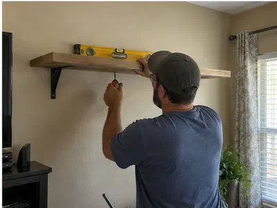 Handyman leveling and fastening a wood wall shelf in a family room