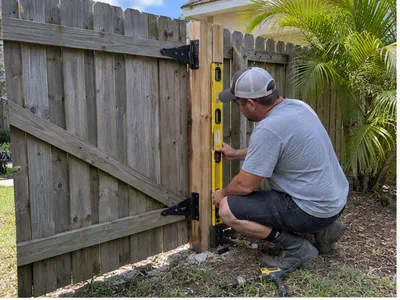 Handyman checking the hinge post on a sagging wooden backyard gate