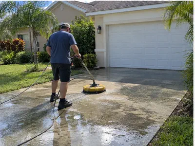 Handyman cleaning algae from a concrete driveway with a round surface cleaner